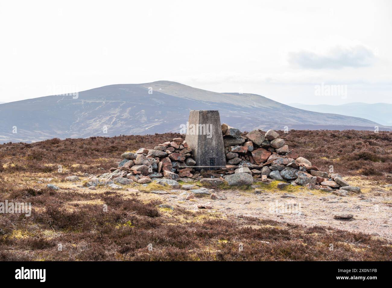 The trig point at the summit of Peter Hill near Finzean, Aberdeenshire, Scotland, with Mount Battock in the background Stock Photo