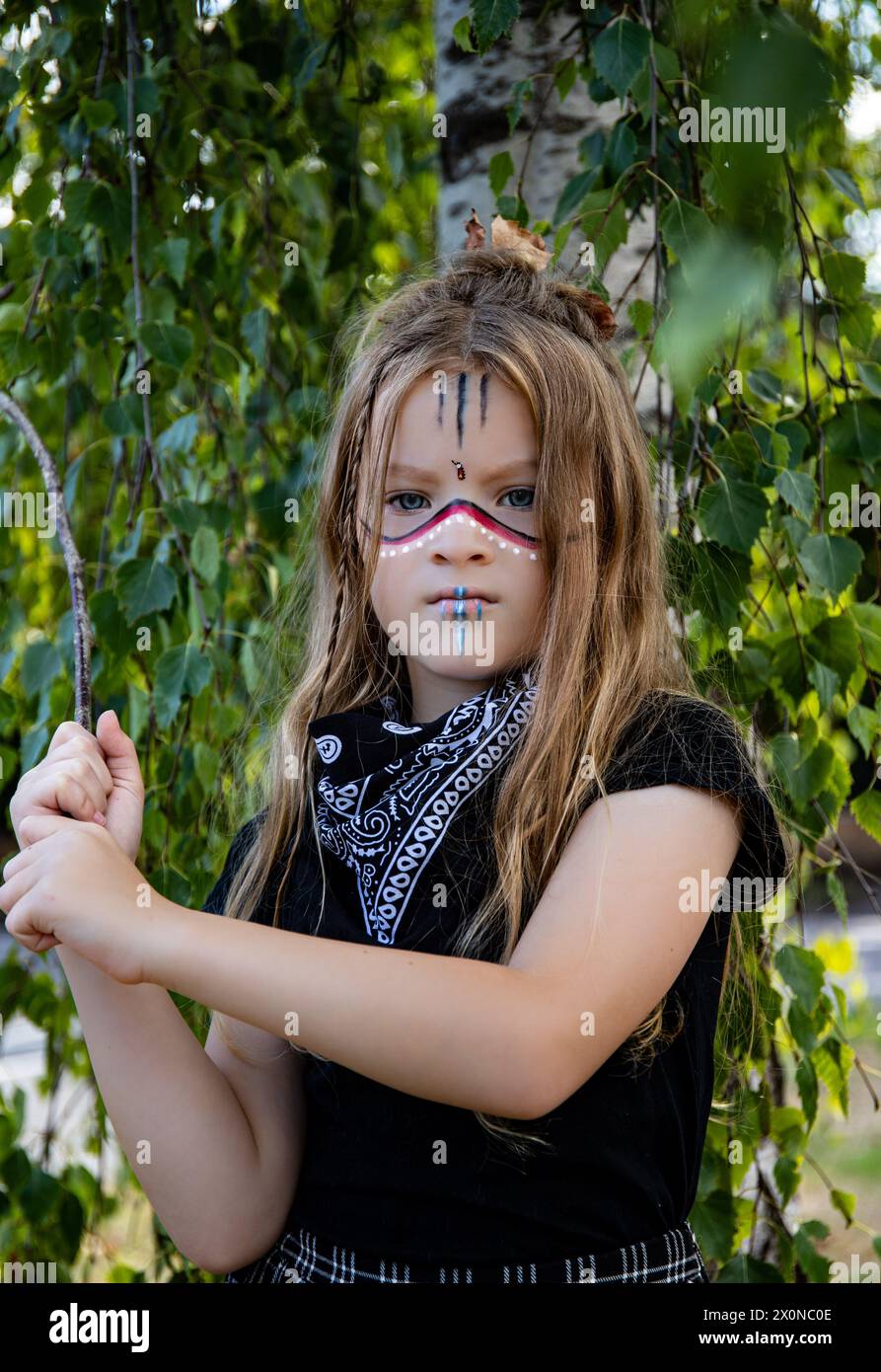 Tribe girl with long hair and traditional makeup dress up school day child holding a stick in the woods Stock Photo