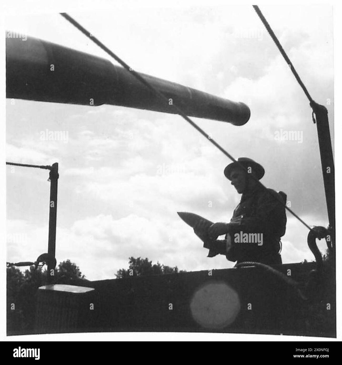 Photograph shows a crew member of a 4-inch naval mobile gun handling a ...