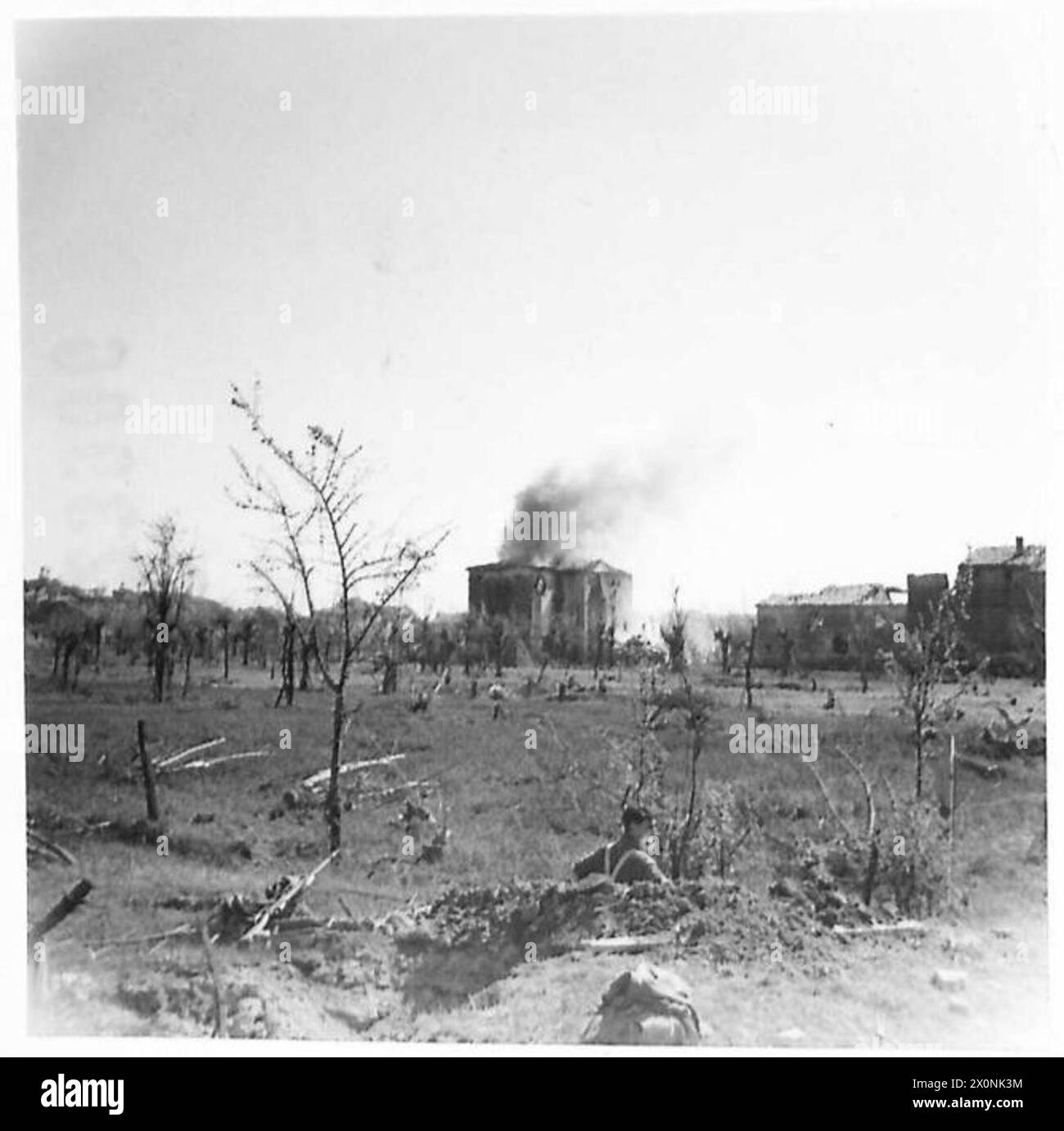 A shell bursts on a house in Cotignola while Eighth Army infantry dig in nearby. Photographic negative captures military operations over the River Senio. Stock Photo