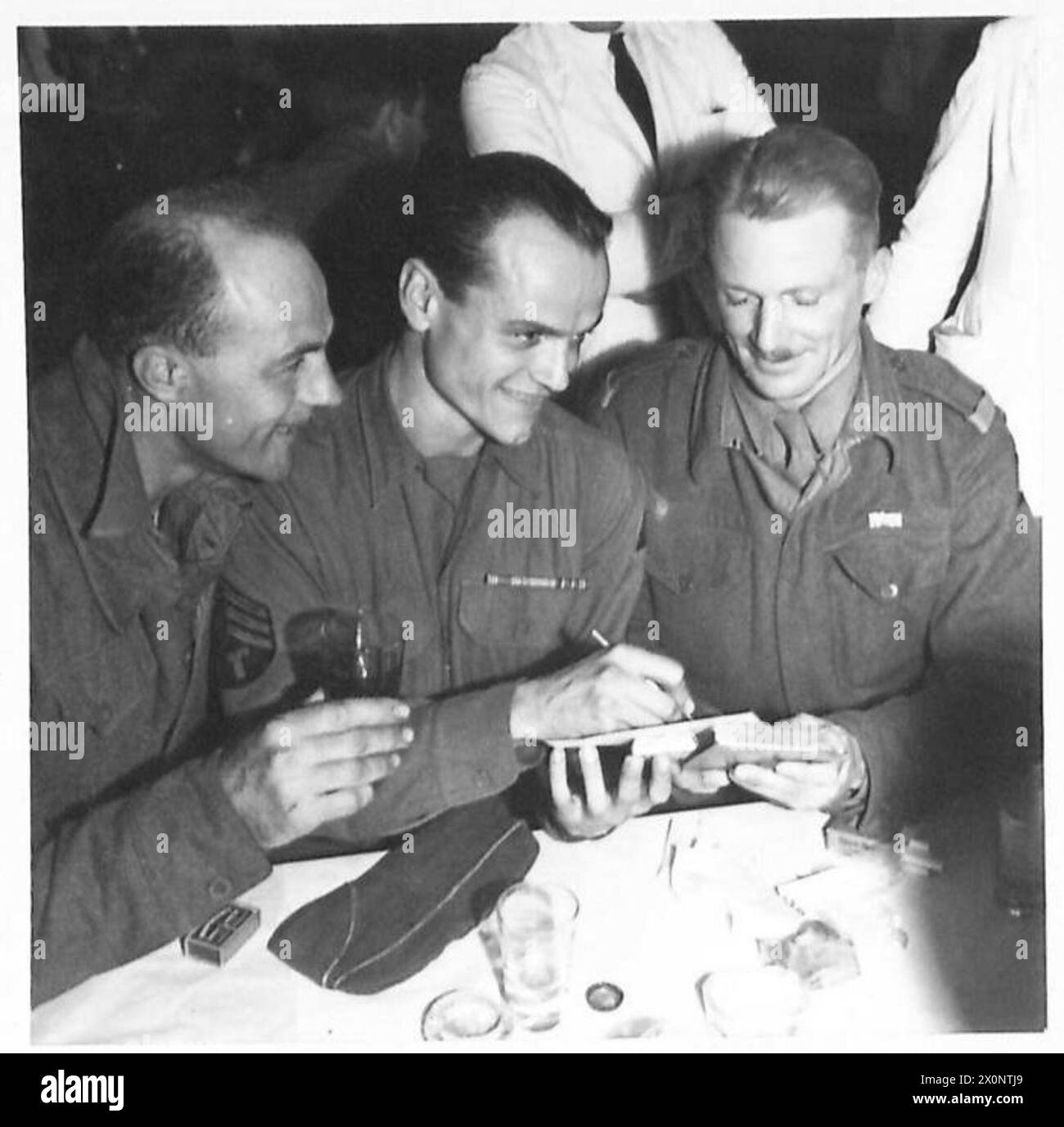 FIFTH ARMY : FIELD MARSHAL ALEXANDER ATTENDS SOLDERS' DINNER - An American soldier autographs a comrade's menu. Left to right:- Gnr. R. Westlake of Springs, Transvaal; Sgt. Bob Yates of Los Angeles, California, Sgt. Major D.L. Clamp of Johannesburg. Photographic negative , British Army Stock Photo