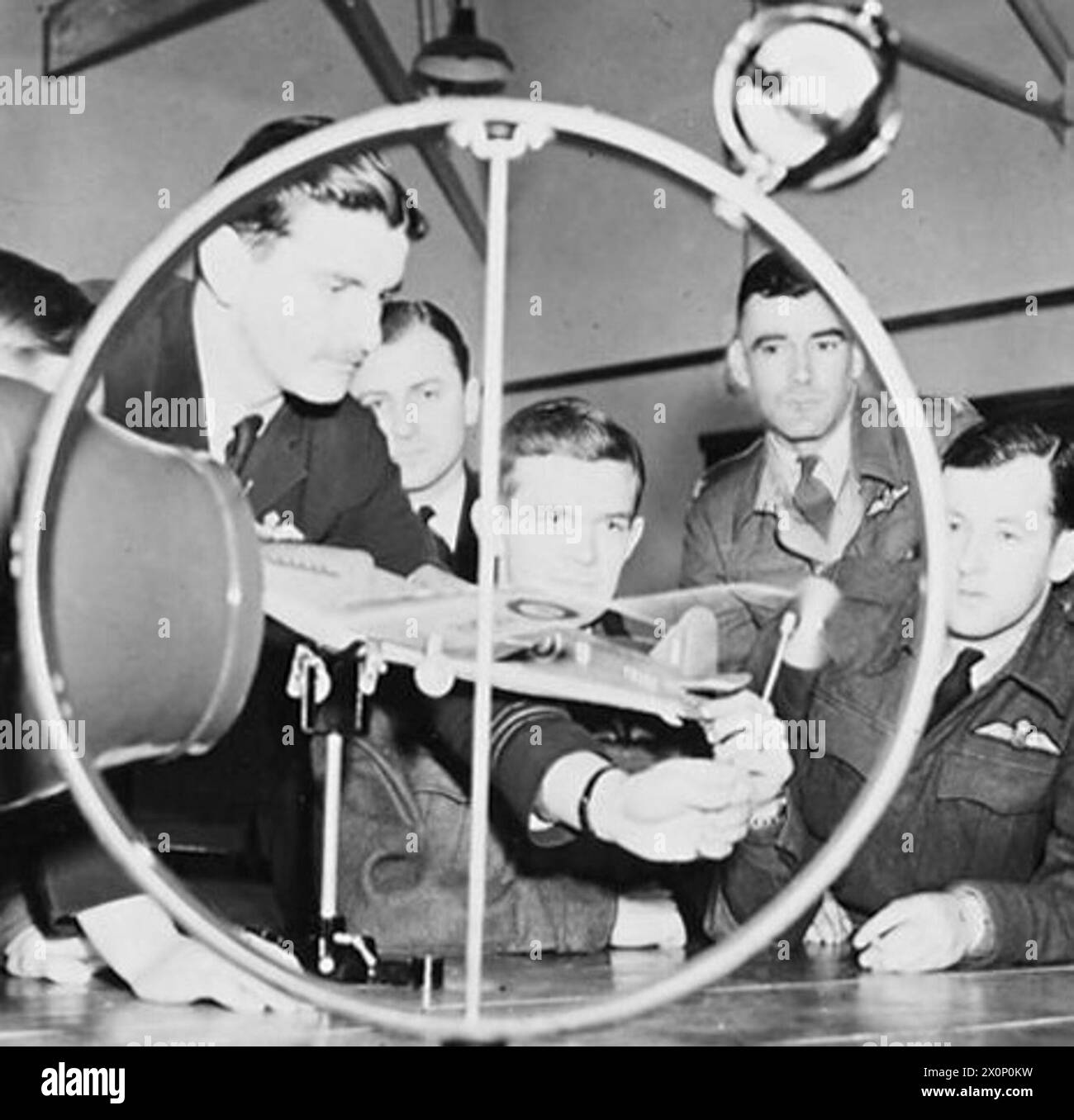 EMPIRE CENTRAL FLYING SCHOOL : AIR UNIVERSITY OF THEALLIED NATIONS. - (Picture issued 1943) For story see CH.8186. Officers at the E.C.F.S. studying how air flows past an aircraft in flight. A wind tunnel mounted on the bench provides an air stream over the model aircraft, which can be tilted to various flight altitudes. The flow over the wings is demonstrated by the behaviour of the tufts of wool on their upper surfaces. The wing-tip air-vortices are shown by the spinning of the small windmill held by the Australian wing commander. Photographic negative , Royal Air Force Stock Photo