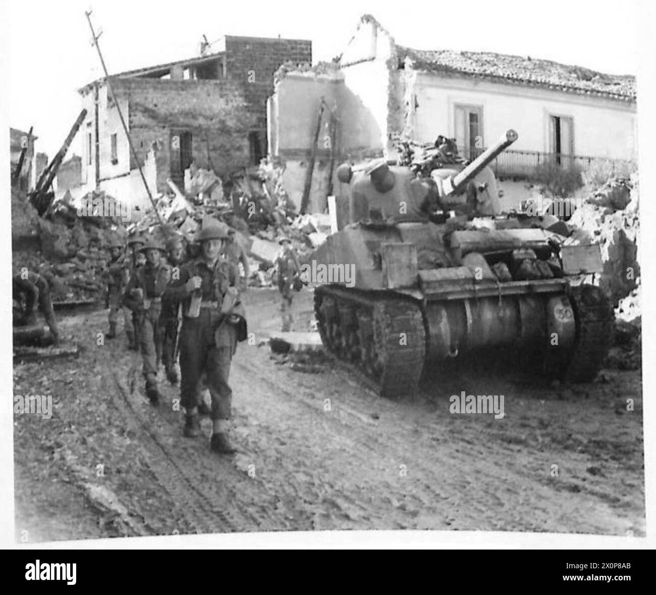 Men of 1/5 Queen's march past a Sherman tank through the ruins of ...