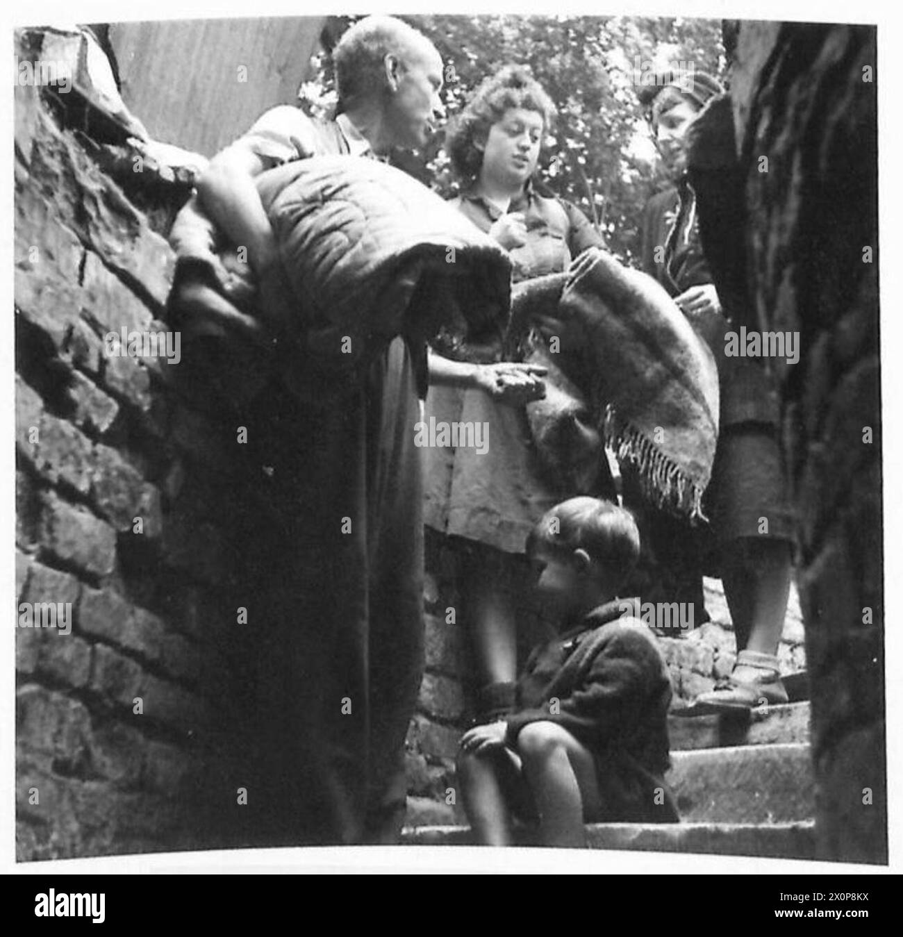AN UNDERGROUND SHELTER IN CAEN - With their blankets ready for the stay in the shelter a family stop for a talk before going down into the shelter. Photographic negative , British Army, 21st Army Group Stock Photo