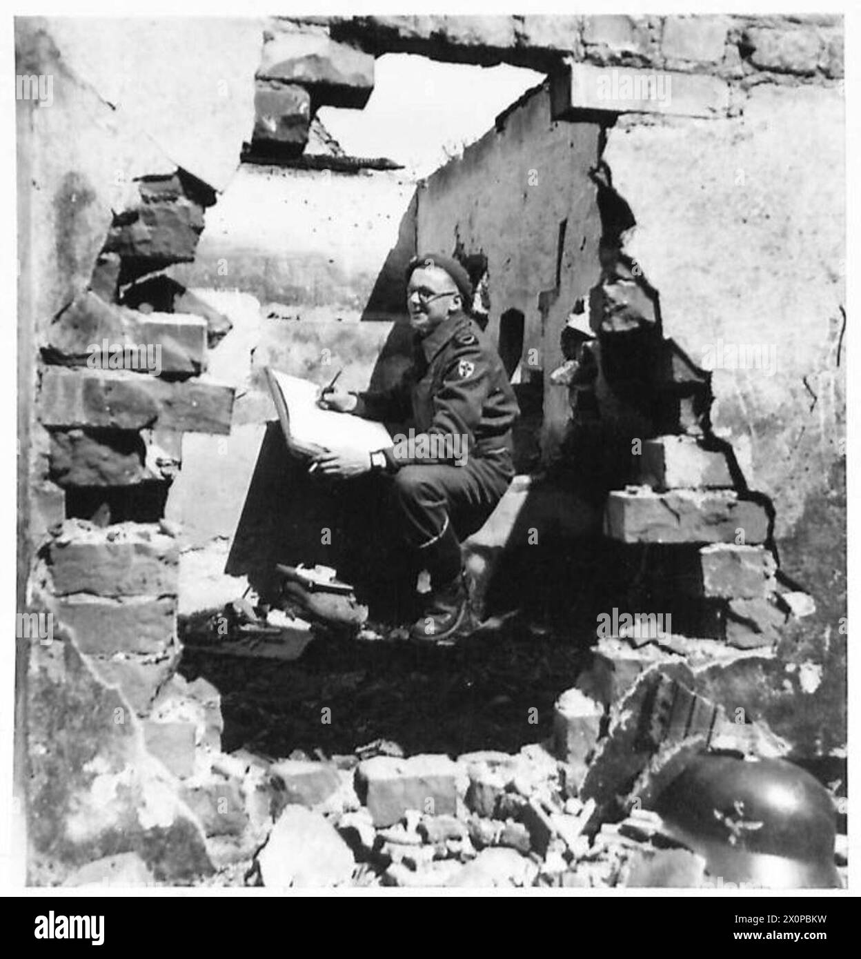 GILES IN GERMANY - He sits among the ruins of a German farmstead and makes a background for one of his cartoons. Photographic negative , British Army, 21st Army Group Stock Photo