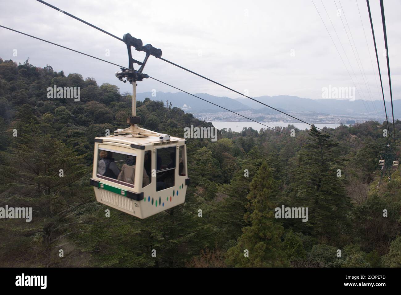 A cable car is suspended in the air, with a view of the mountains and a lake below Stock Photo