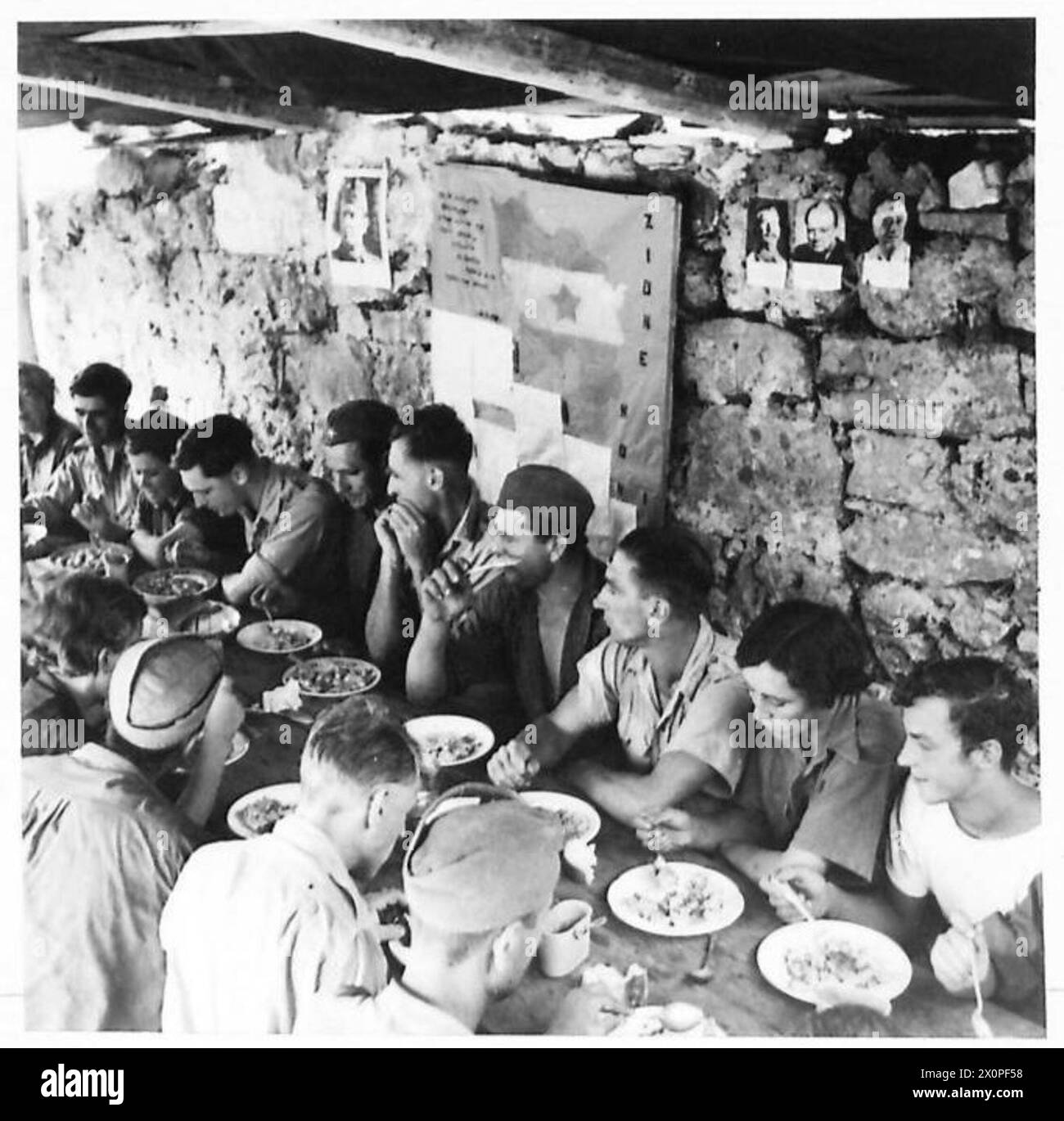 THE BRITISH ARMY IN THE ADRIATIC, 1944-1945 - Surgeons of the Royal Army Medical Corps eating a meal with communist Partisans, both male and female, on the island of Vis off the coast of Yugoslavia, August 1944. Note portraits of Tito, Stalin, Churchill and Roosevelt on the wall British Army, British Army, Royal Army Medical Corps, Yugoslav Army Stock Photo