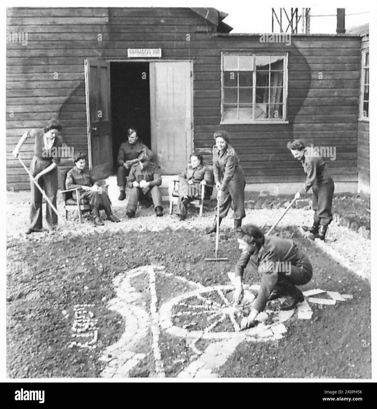 RECREATION HUTS ON GUN SITES - A.T.S. attending to the garden and Royal Artillery badge which they have laid in front of the Barbados hut. Photographic negative , British Army Stock Photo