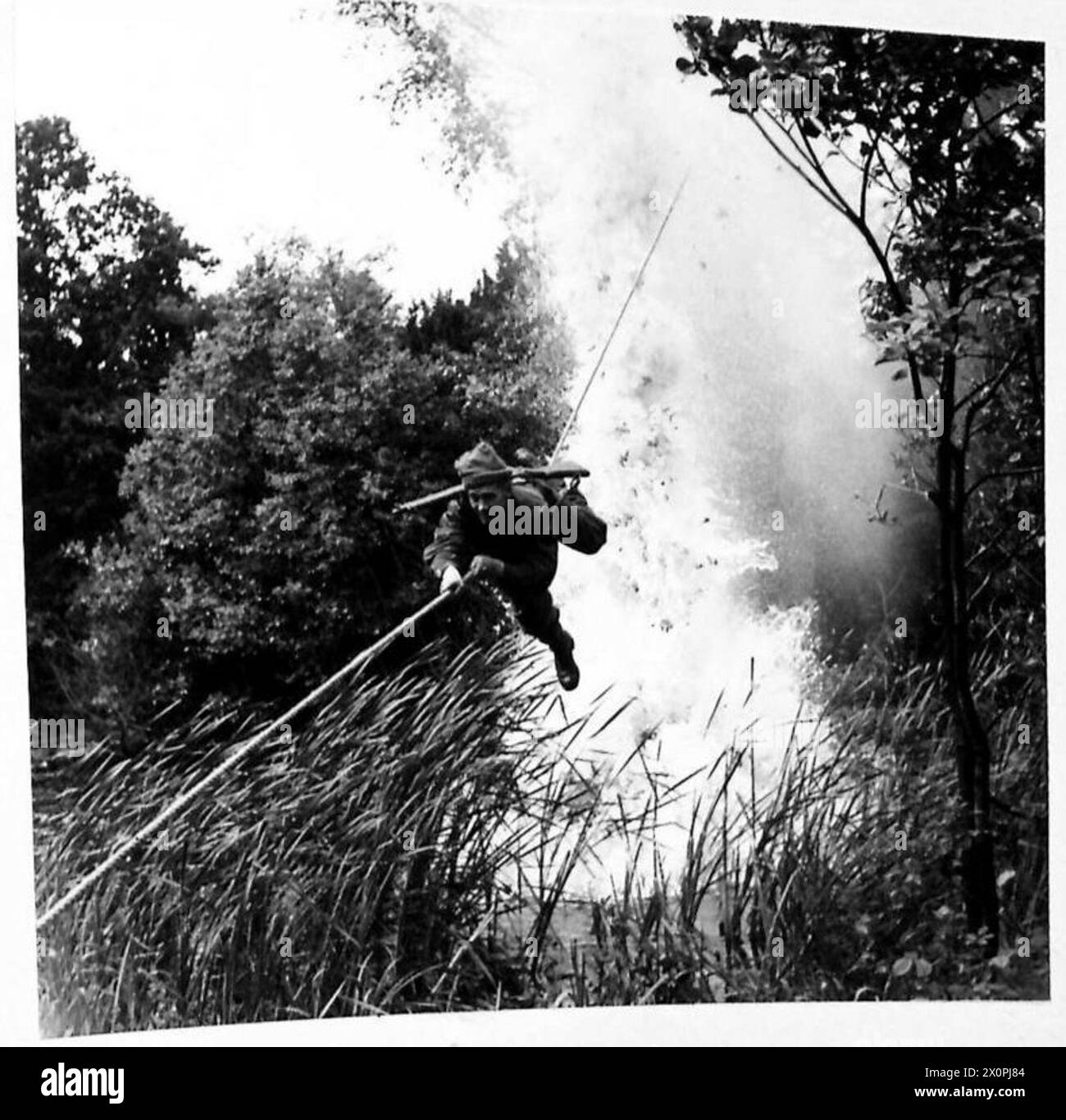 THE EAST YORKSHIRES TOUGHEN UP - The Death Slide : A soldier, with the aid of a Toggle-Rope, slides down a rope attached across a river under 'enemy fire'. Photographic negative , British Army Stock Photo