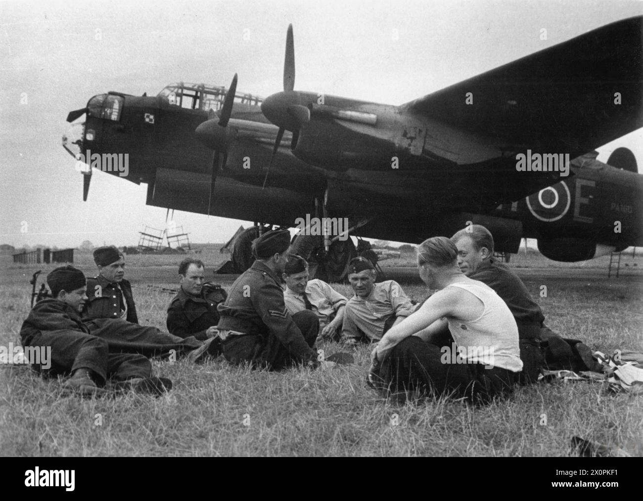 THE POLISH AIR FORCE IN BRITAIN, 1940-1947 - Ground mechanics of No. 300 Polish Bomber Squadron enjoying a short break in the open air after making their Avro Lancaster bombers ready for a next sortie. Note the Lancaster BH-E, PA160 in the background.Photograph very likely taken at RAF Faldingworth, summer 1944 Polish Air Force, Polish Air Force, 300 'Land of Masovia' Bomber Squadron Stock Photo