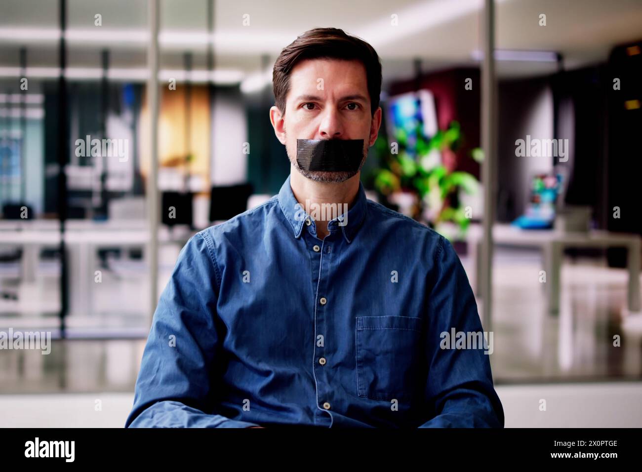 Young Man With Black Duct Tape Over His Mouth In Office Stock Photo