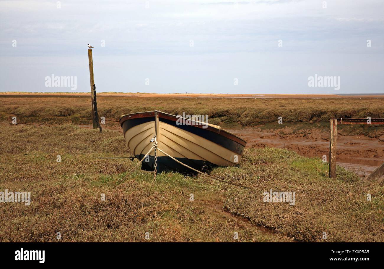 A dinghy on salt marshes by the tidal channel and harbour on the North Norfolk coast at Thornham, Norfolk, England, United Kingdom. Stock Photo