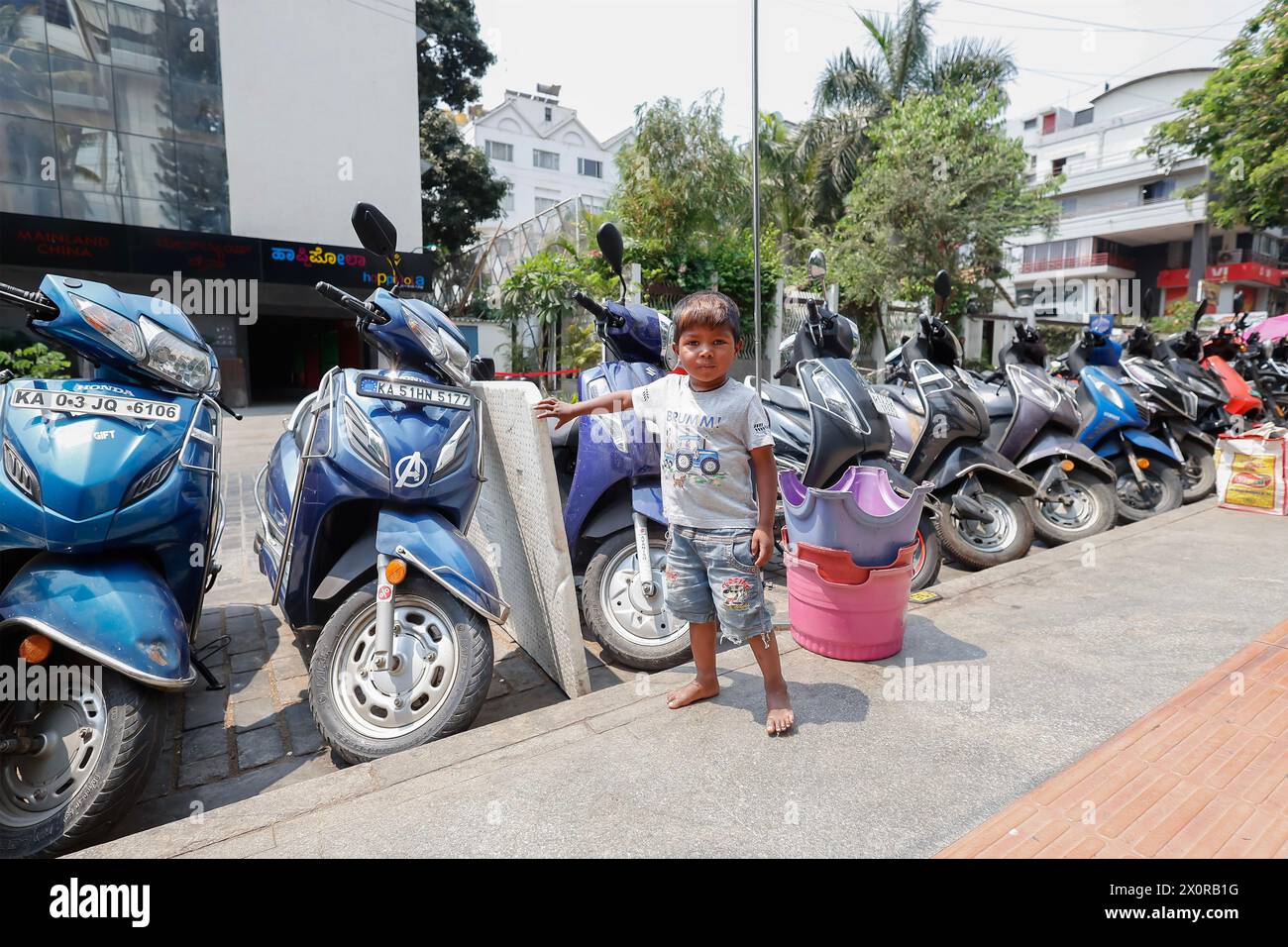 Young boy (3-4) standing next to a row of motorbikes in Church Street, Bangalore, Bengaluru, Karnataka, India Stock Photo