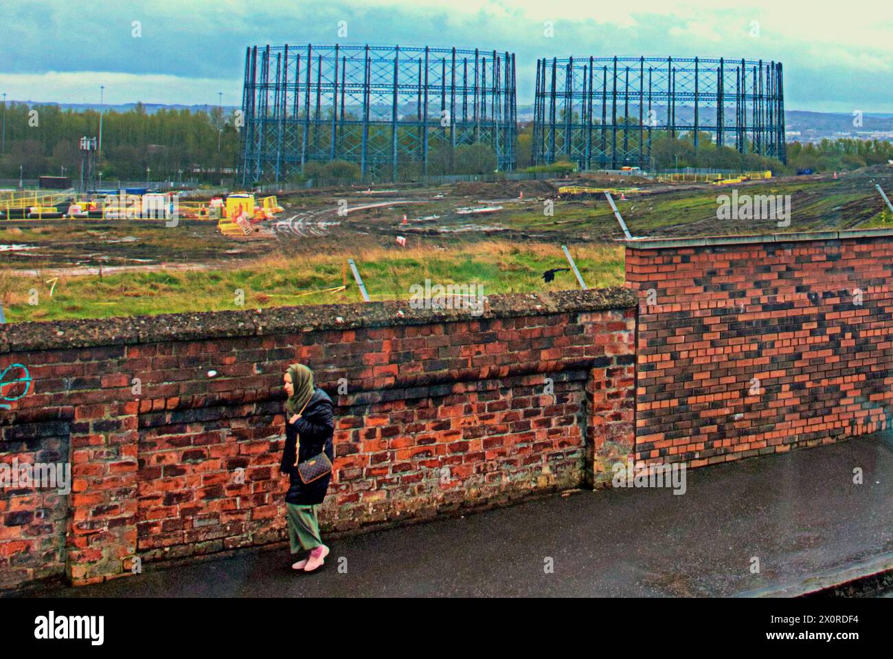 Glasgow, Scotland, UK. 13h April, 2024: UK Weather:  Provan Gas Works  Blackhill, Blochian, Germiston and Provanmill   Wet and Windy in the city as a local strides with the gasometers in the north of the city, Buchanan Street. Credit Gerard Ferry/Alamy Live News Stock Photo