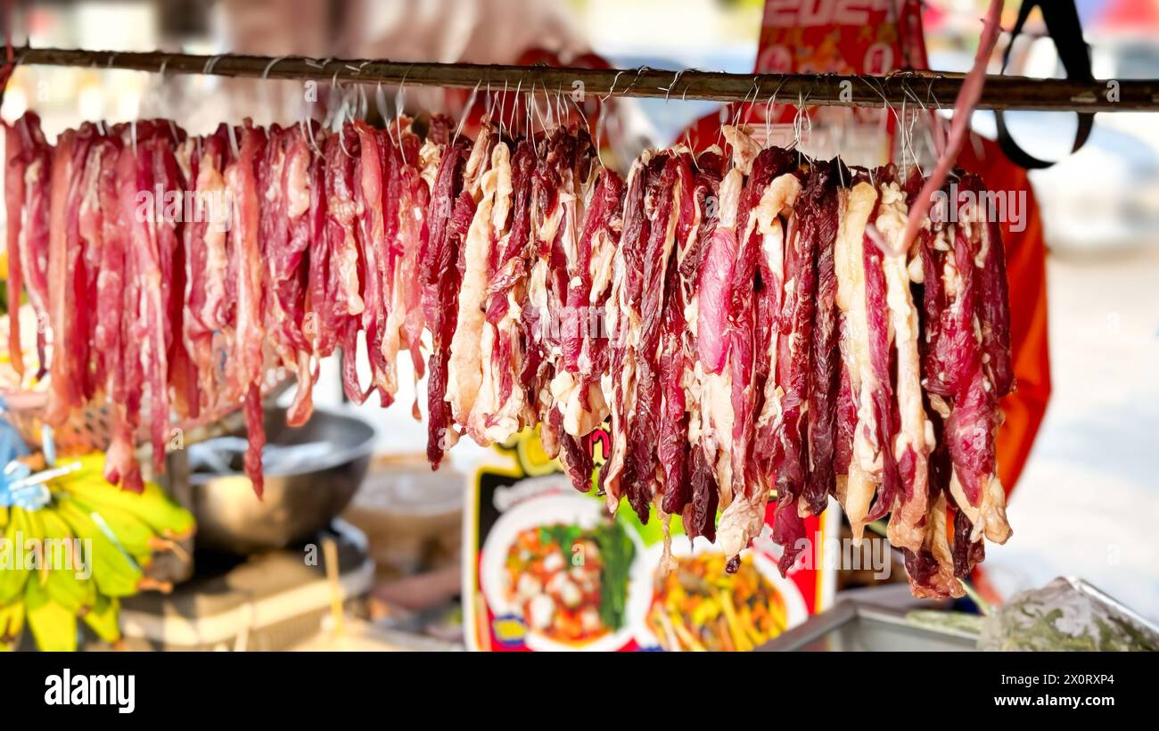 Dried meat hangs in an open-air market, a rustic Asian delicacy offered amidst a backdrop of fresh produce, inviting passersby to indulge in local cul Stock Photo