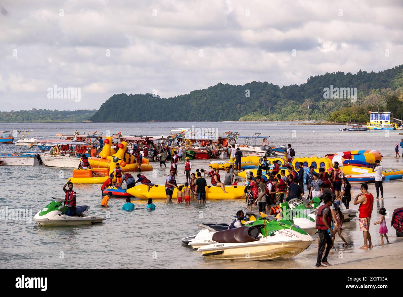 The beach is dotted with colorful inflatable boats and banana boats, with people on board enjoying the water. Stock Photo