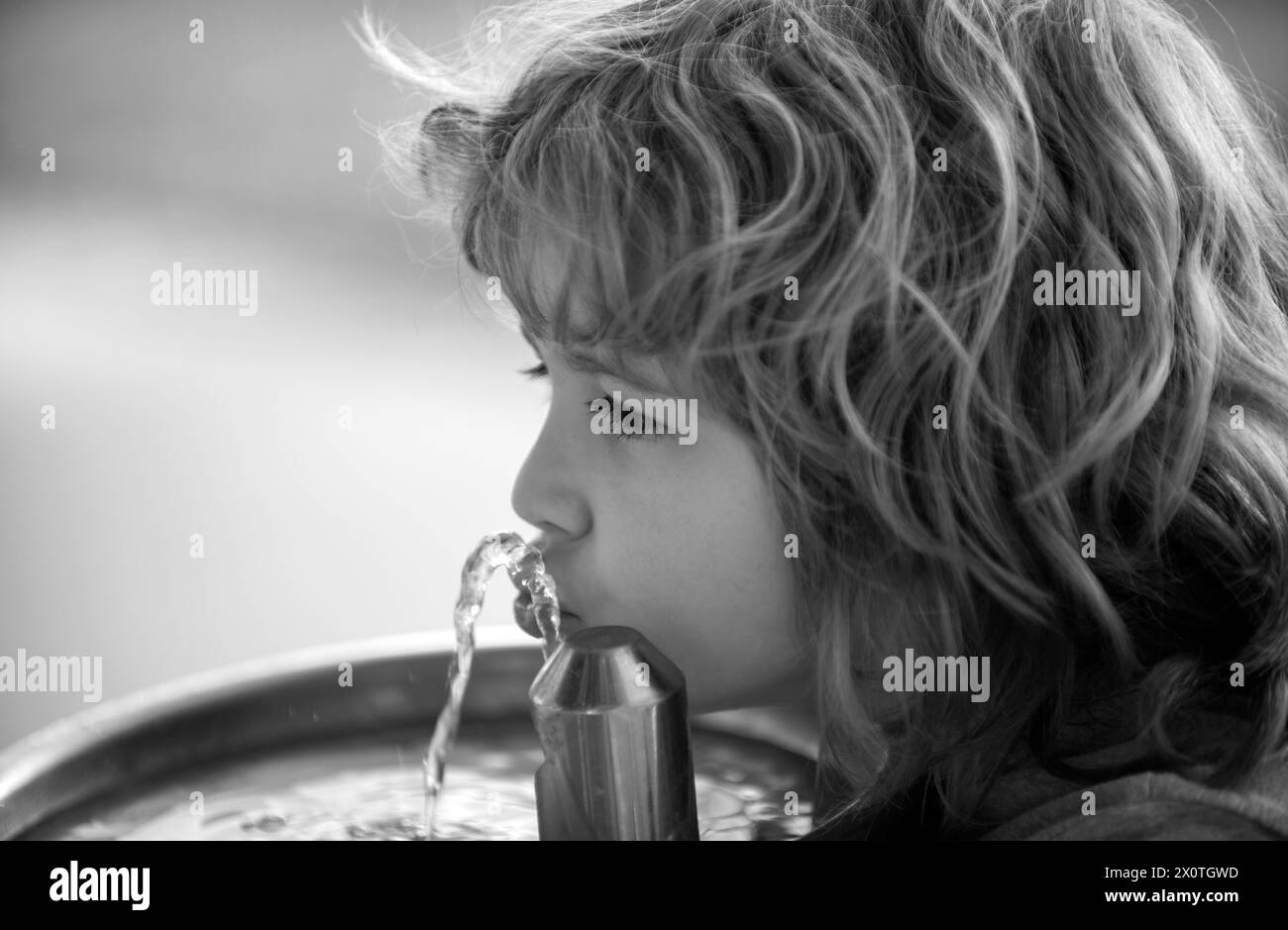 Child drinking water from a water fountain in park outdoor. Stock Photo