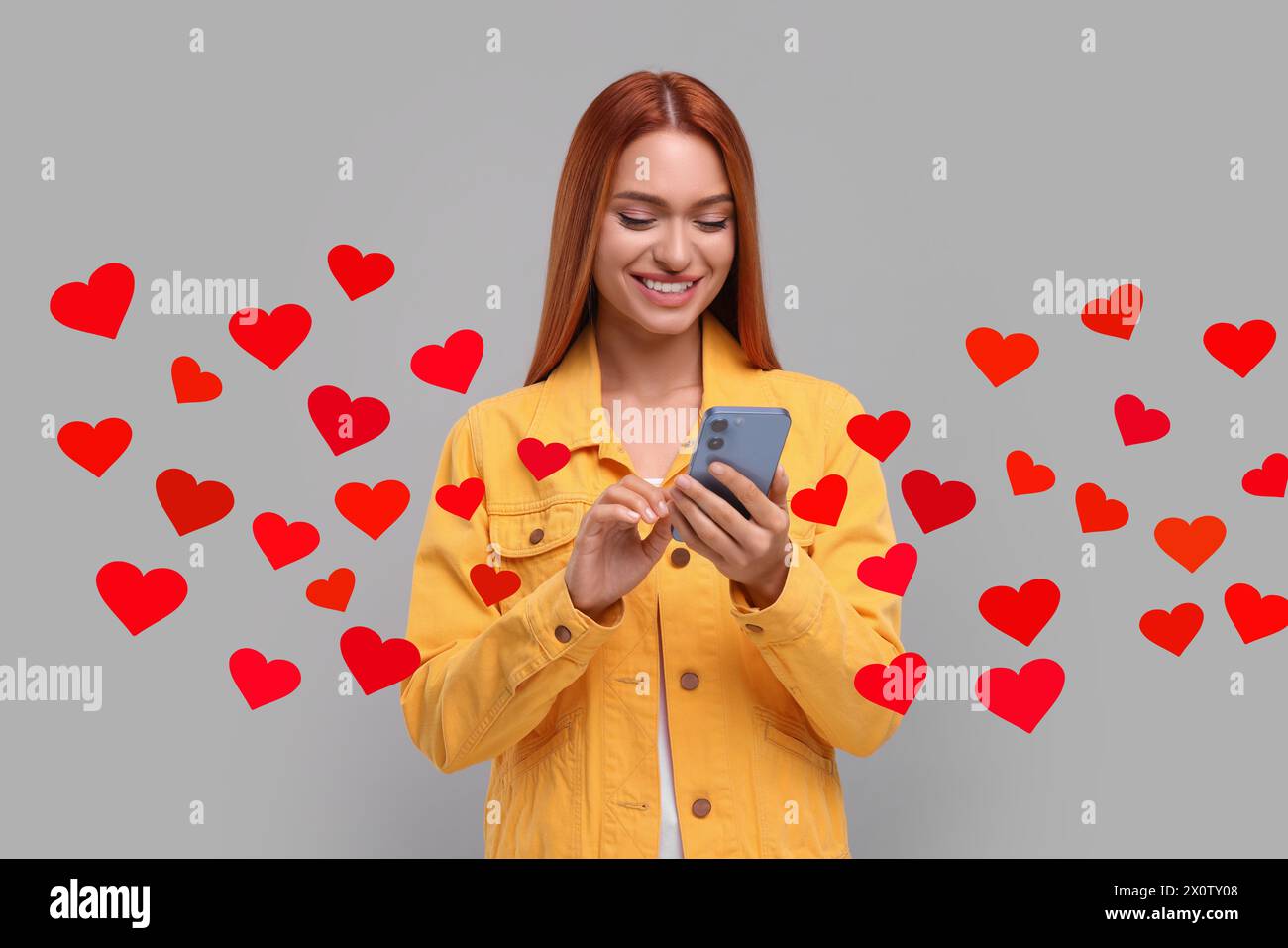 Long distance love. Woman chatting with sweetheart via smartphone on grey background. Hearts flying out of device and swirling around her Stock Photo