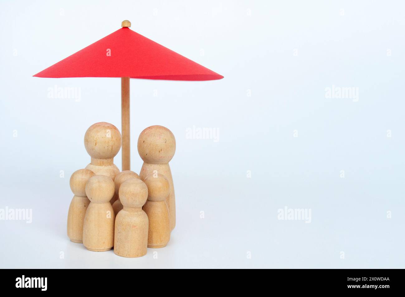 Red toy umbrella and wooden family doll figures a white background. Life insurance coverage concept. Stock Photo