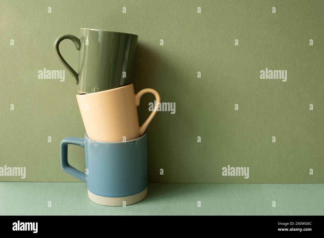 Stack of ceramic mug cups on green table. khaki wall background Stock Photo