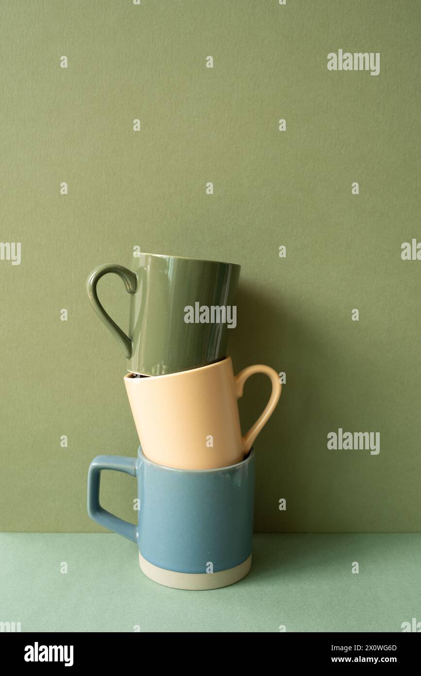 Stack of ceramic mug cups on green table. khaki wall background Stock Photo