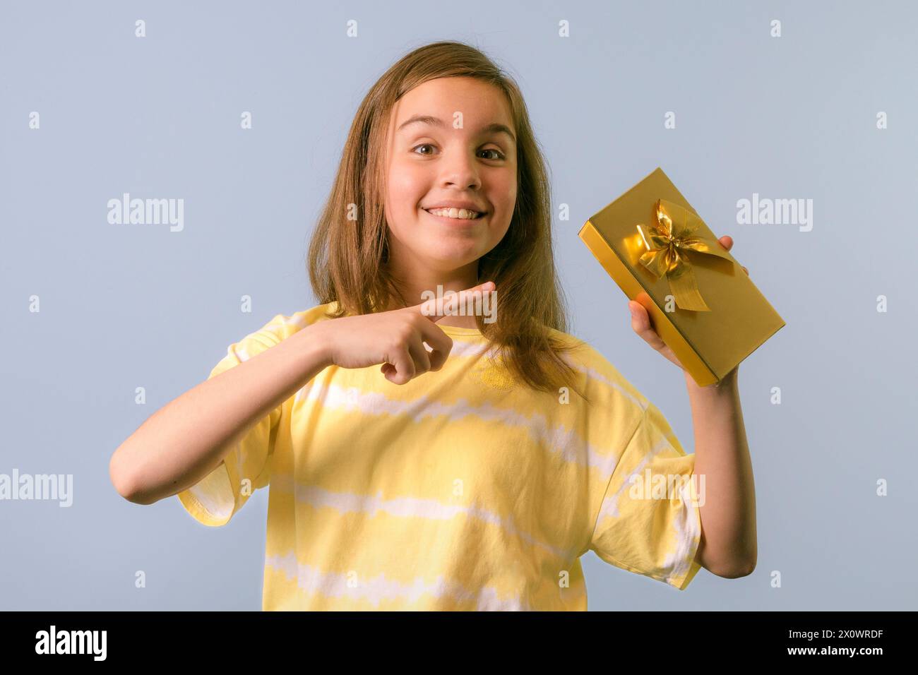 Joyful girl with a gift in her hand. A teenager rejoices at a gift in a gold box. Unexpected surprise Stock Photo