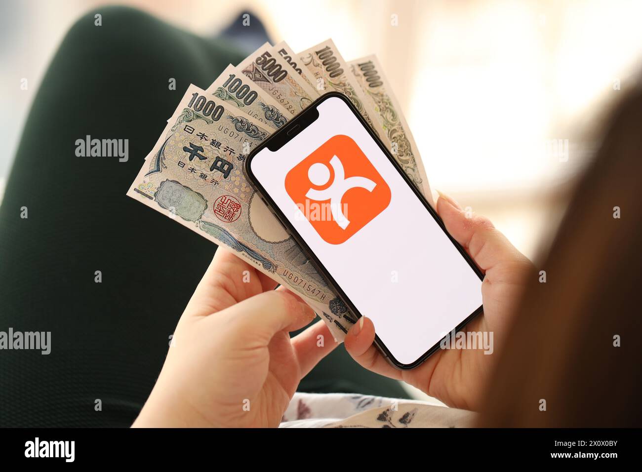 KYIV, UKRAINE - APRIL 1, 2024 Dianping platform icon on smartphone screen and money in female hand. iPhone display with app logo and japanese yen money bills in women hands close up Stock Photo
