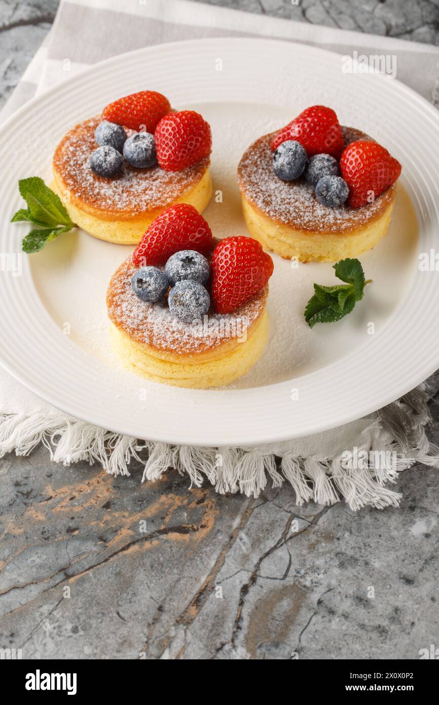 Japanese style sluffy souffle pancake dessert with blueberry and strawberry close-up on a plate on the table. Vertical Stock Photo