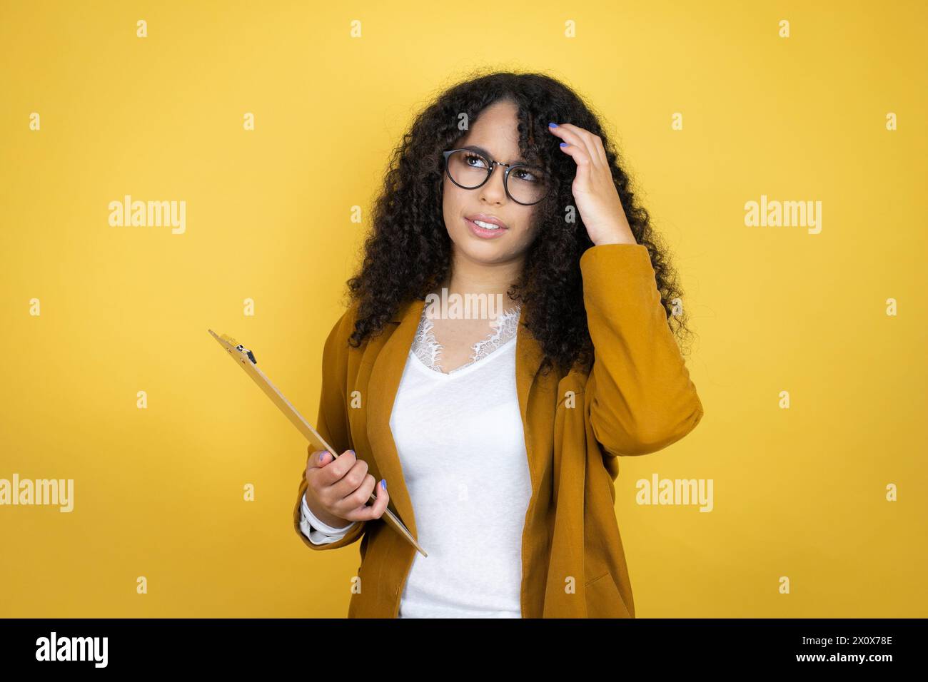 African american business woman with paperwork in hands over yellow background confuse and wonder about question. Uncertain with doubt, thinking with Stock Photo