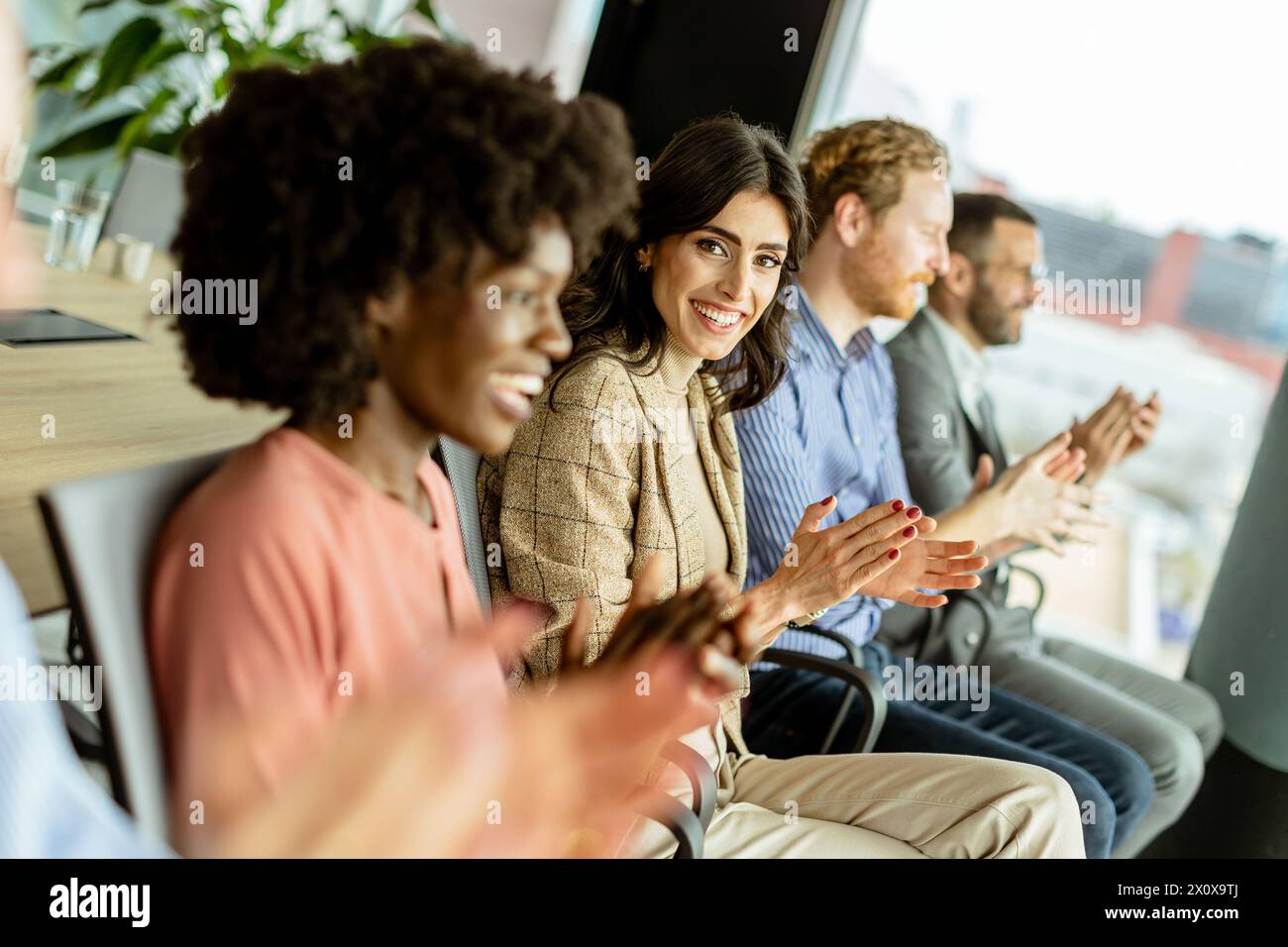 Smiling woman leads a round of applause with peers, sharing a moment of joy Stock Photo