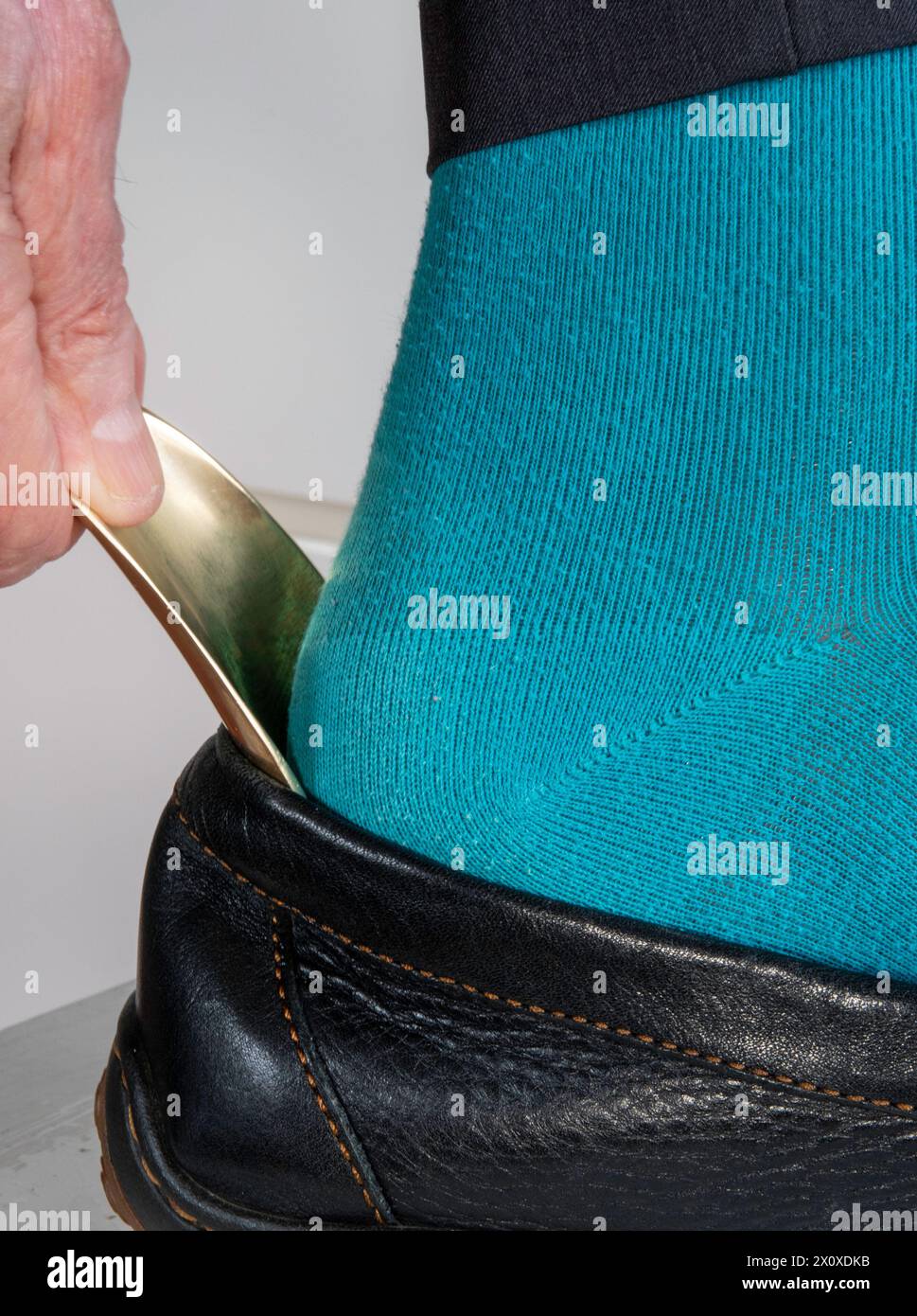 Mature man uses a shoehorn to easily slide his foot into his shoe, 2024