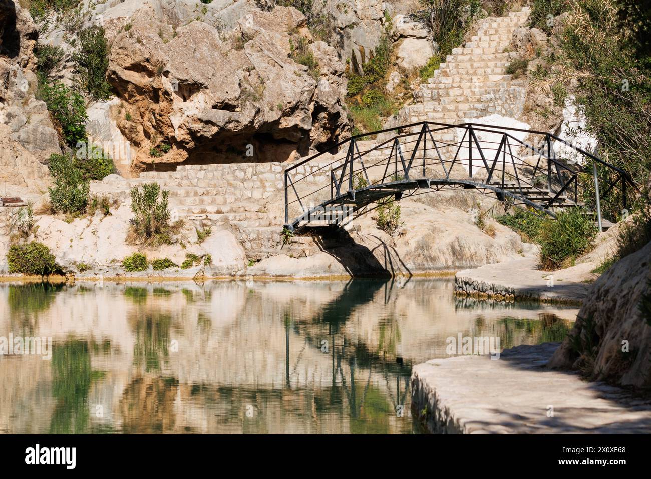 Wrought iron bridge in natural pool of the municipality of Bolbaite with reflections in the water, Spain Stock Photo