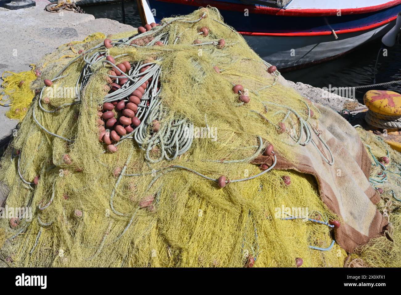 Yellow fishing net with buoys placed on the pier in front of fishing boat. There is lot of copy space. Stock Photo