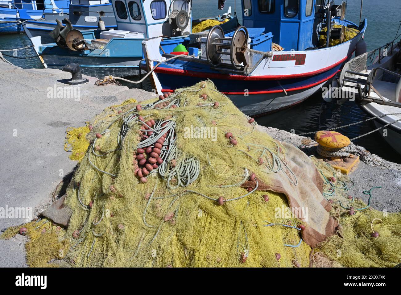 Yellow fishing net with brown buoys placed on the pier in front of fishing boats. There is lot of copy space. Stock Photo