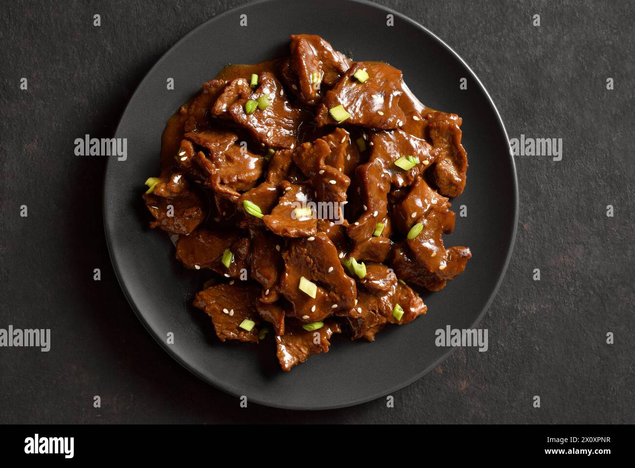 Close up view of asian style beef with soy sauce, green onion and sesame seeds on plate over dark stone background. Top view, flat lay Stock Photo
