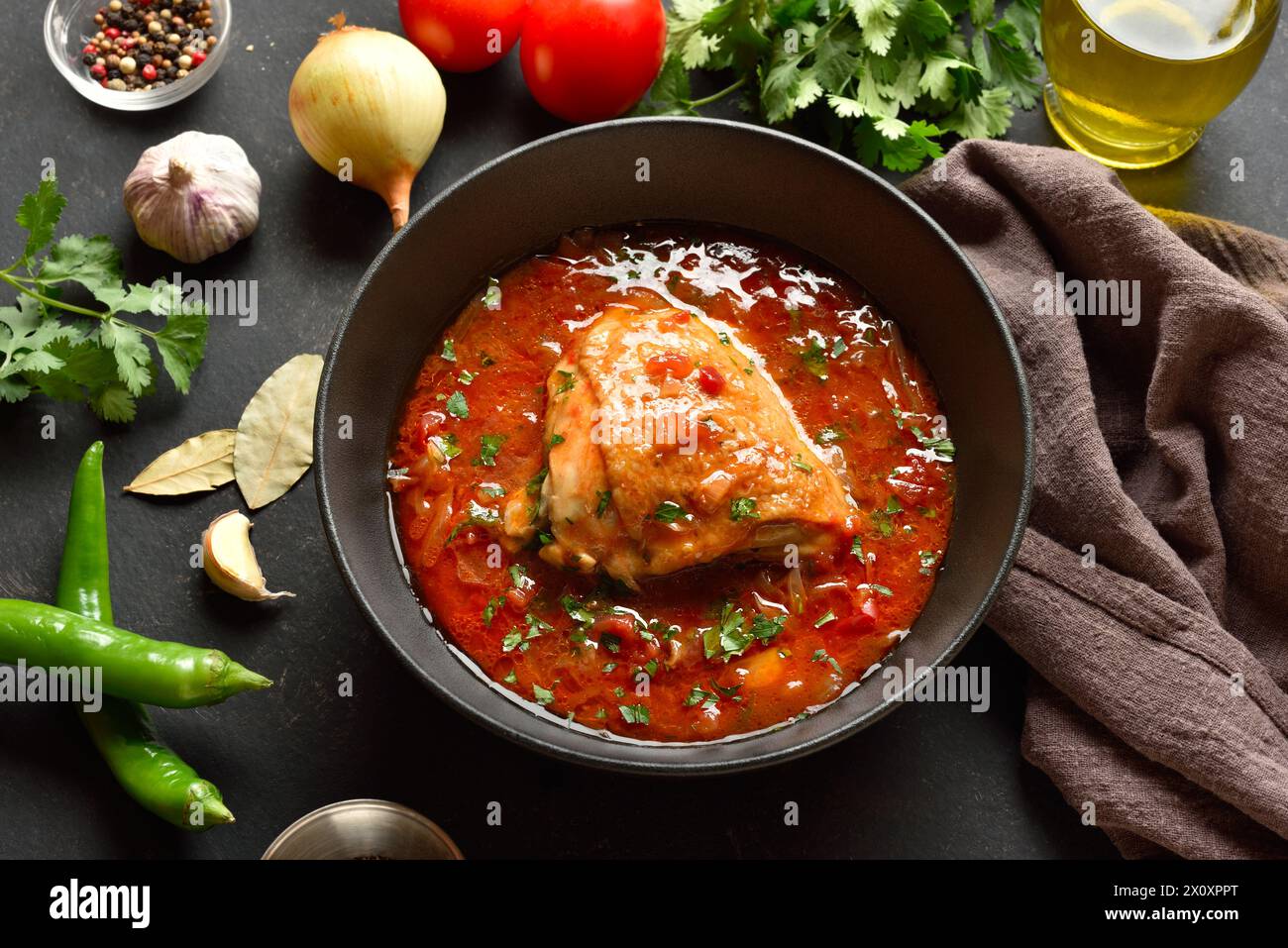 Baked chicken with tomato gravy and herbs in bowl over dark stone background. Tasty homemade chicken stew for dinner. Close up view Stock Photo