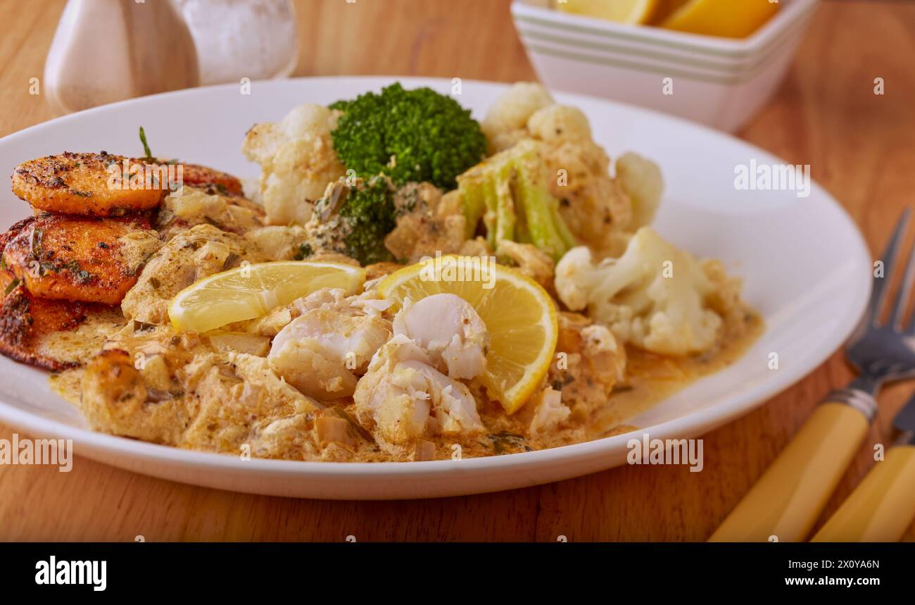 Curried lemon fish fillets in a lemon sauce with vegetables and fried sweet potato discs. Stock Photo
