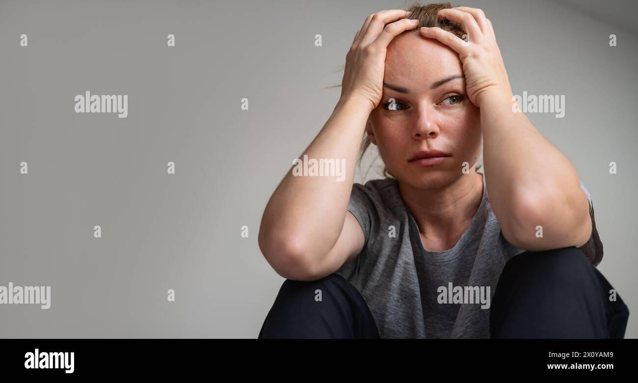 Portrait of downcast and depressed adult woman at home. Depressed female holding head in her hands. Stock Photo