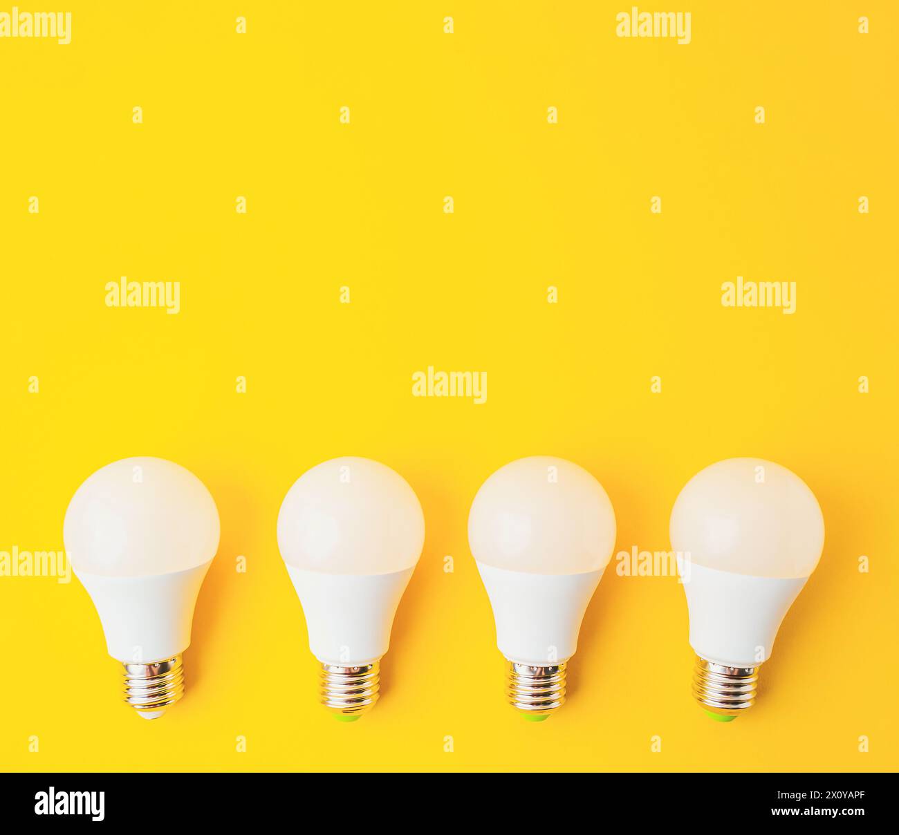 Four white light bulbs are arranged on a yellow background. The bulbs are all the same size and shape, and they are evenly spaced out. Concept of unif Stock Photo
