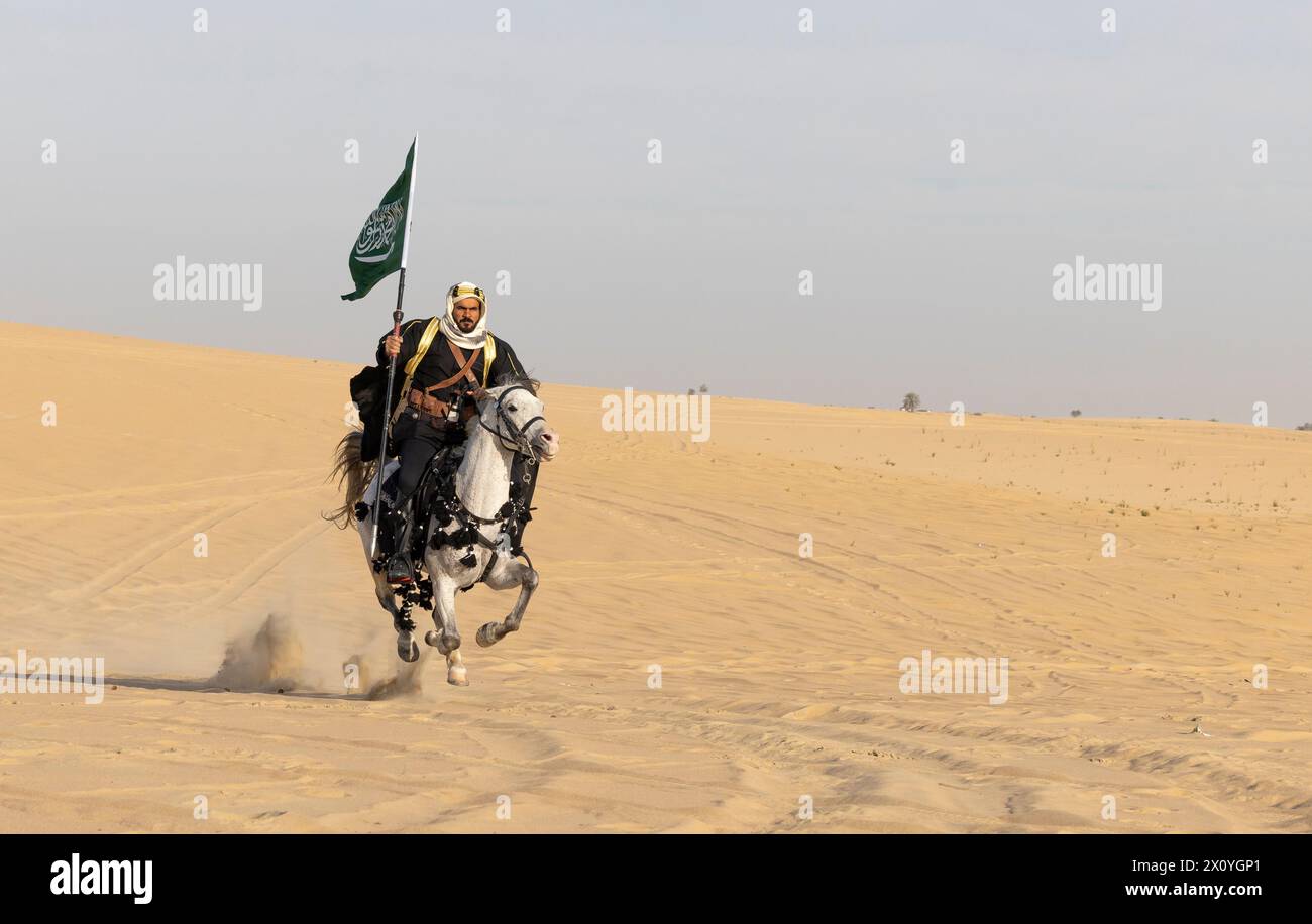 Saudi man in traditional clothing with his white stallion, riding with a saudi flag in his hand Stock Photo