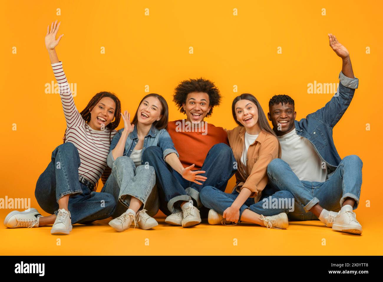 Friends sitting and raising hands joyfully on orange background Stock Photo