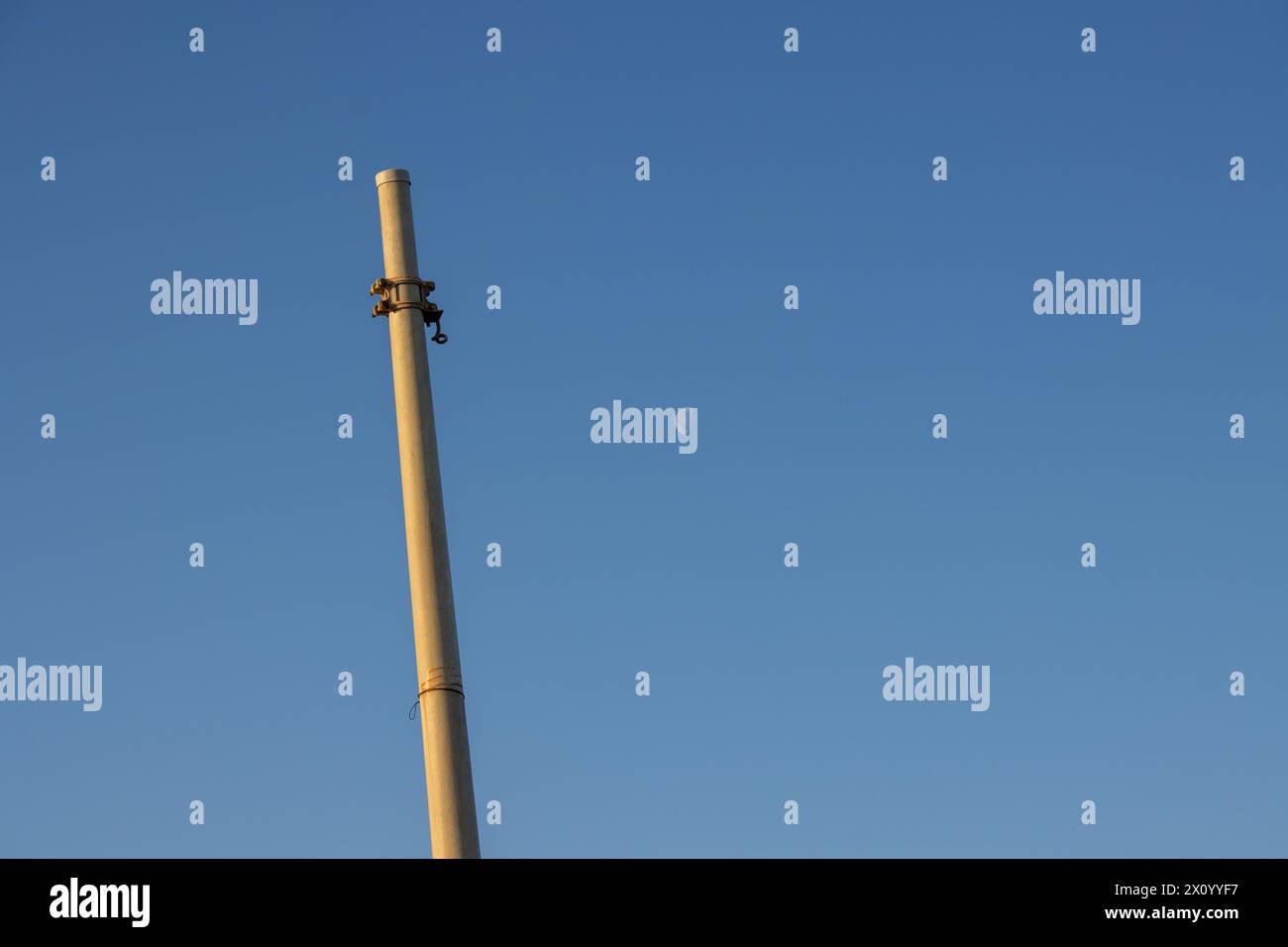 Column in the morning sunlight, colored into golden. No lamp or cable, just the pole. Bright blue sky in the background, with a moon in a half. Marsal Stock Photo
