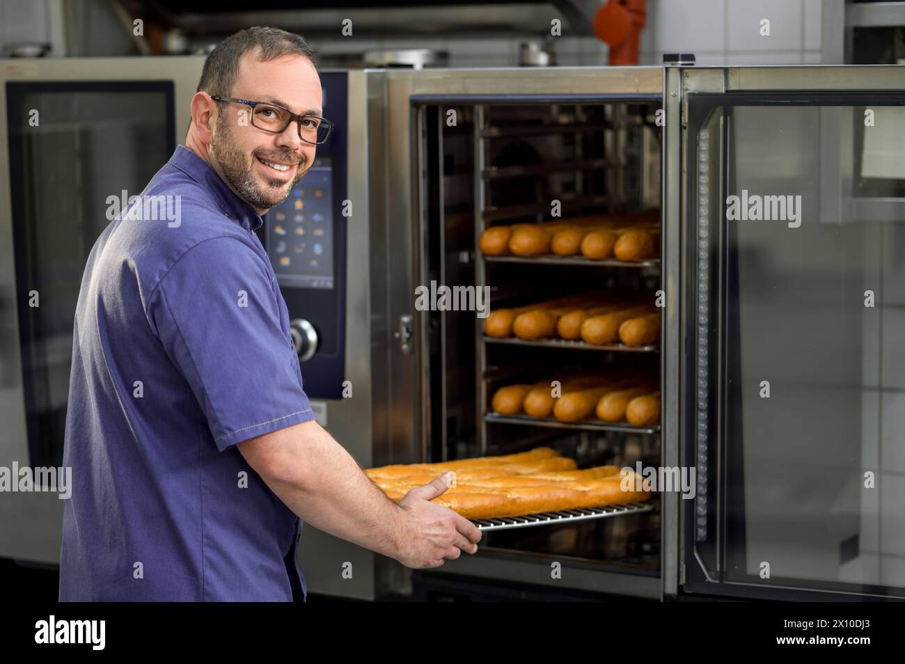 Baker in kitchen near oven with baguettes in bakehouse Stock Photo - Alamy