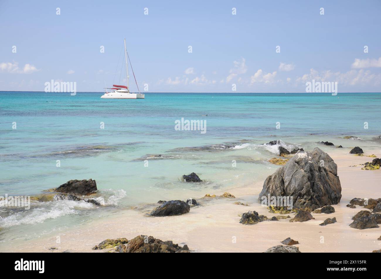 A small boat is sailing in the ocean near a rocky shore. The water is calm and the sky is clear Stock Photo