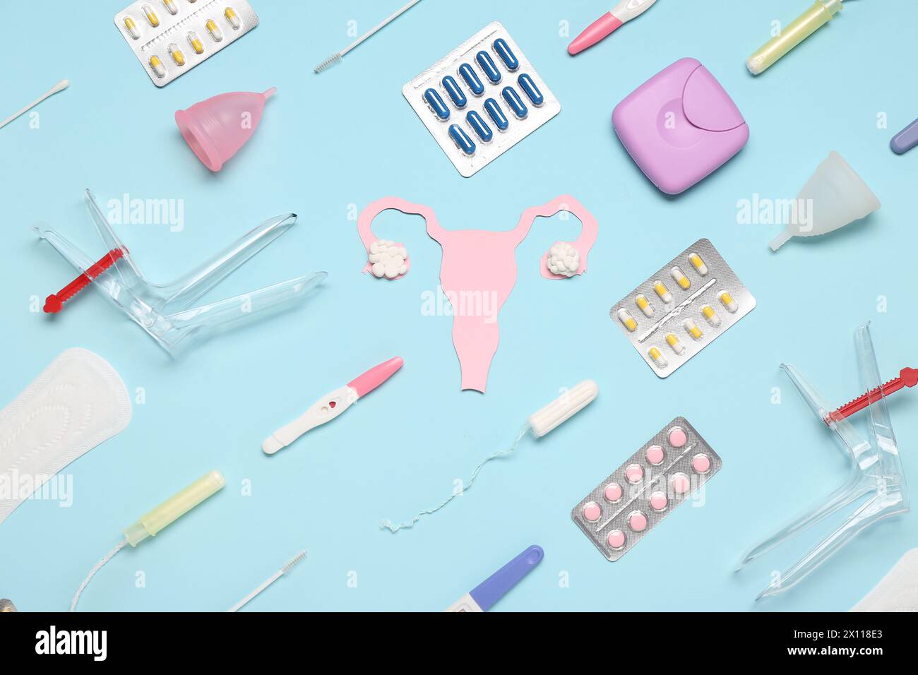 Paper uterus with gynecological speculums, pills, tampons and menstrual cups on blue background Stock Photo