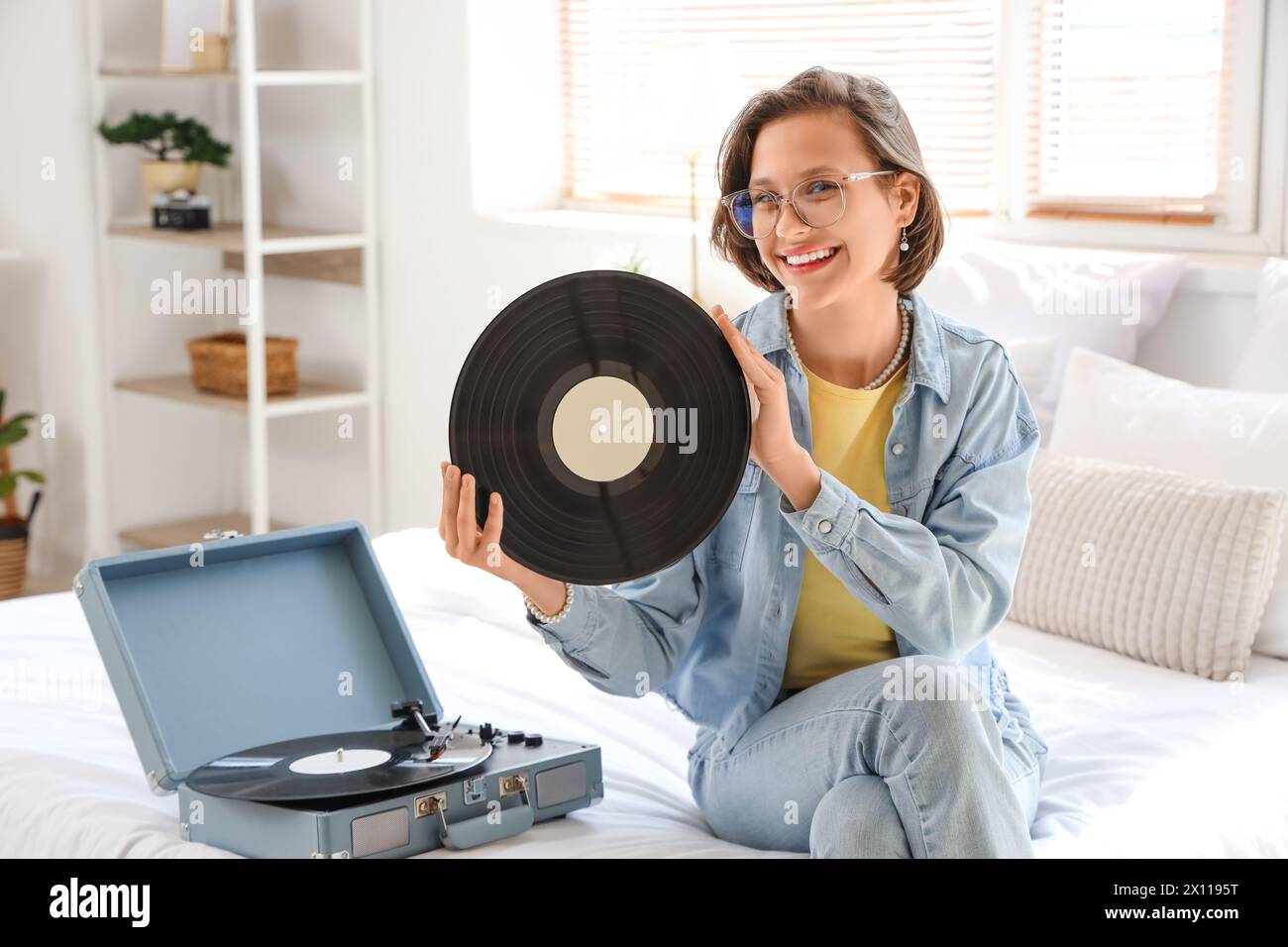 Young woman with vinyl disk and record player sitting in bedroom Stock Photo