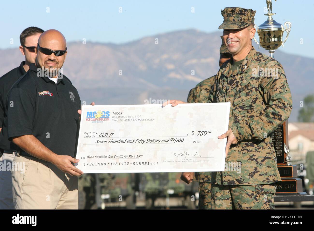 Eddie Bolanos, 46, from Oceanside, Calif., Marine Corps Community Services athletic coordinator (left), presents a first place check in Division III of the 2009 United Services Automobile Association Cup to Col. Bruce E. Nickle, commanding officer of Combat Logistics Regiment 17, 1st Marine Logistics Group (right), during a formation at Camp Pendleton, Calif., Jan. 14, 2010. Stock Photo
