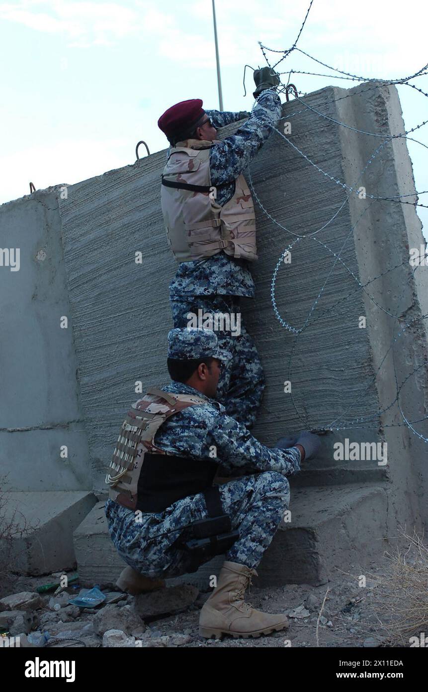 Two Iraqi national policemen with the 1st Battalion, 2nd Brigade, 6th Iraqi National Police place concertina wire near a bridge in Kahdra ca.  2004 Stock Photo