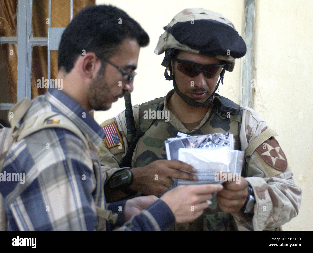 A soldier from 5th Battalion, 20th Infantry Regiment, 3rd Brigade, 2nd Infantry Division (Stryker Brigade Combat Team) and an interpreter review identification papers of a resident while multinational forces search his house in Qabr Abd, a city south of Mosul, during Operation Mayfield III, a cordon and search operation conducted on July 19 2004. Stock Photo