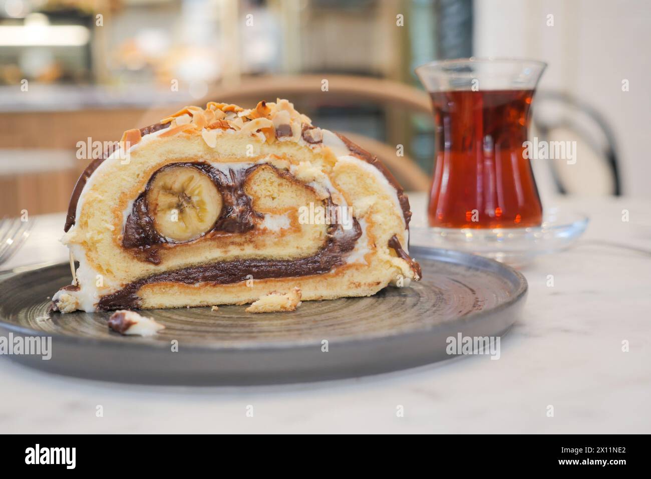 A slice of cake on serveware next to a glass of tea drinkware Stock Photo